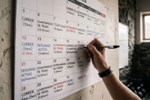 Mano escribiendo un plan de entrenamiento personalizado en un calendario mensual - Saludx10